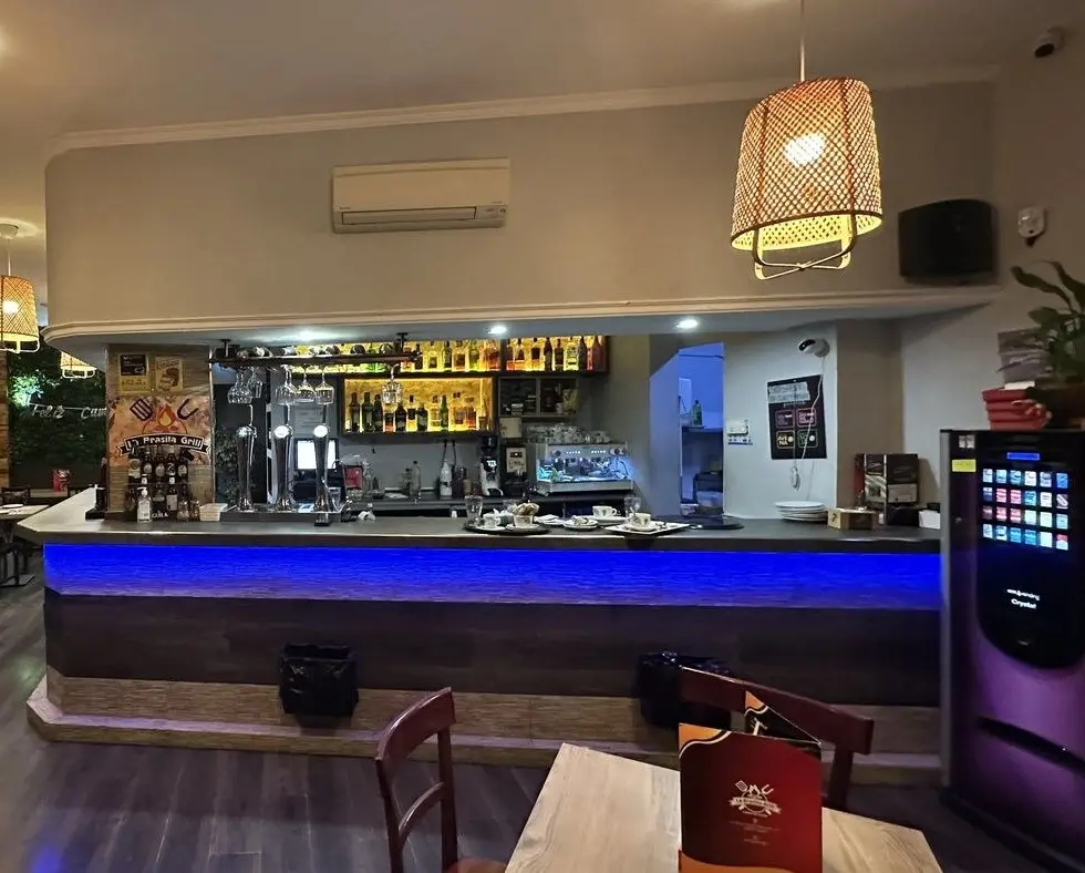 Barra del restaurante con luz azul, botelleros y una lámpara de mimbre, y una mesa de madera en primer plano
