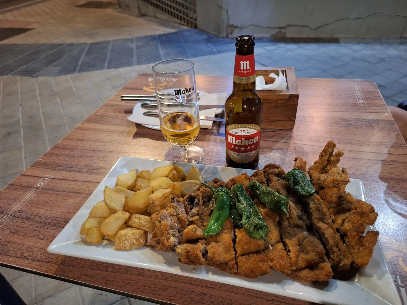 Cachopo cortado en porciones con patatas, pimientos de Padrón y una cerveza